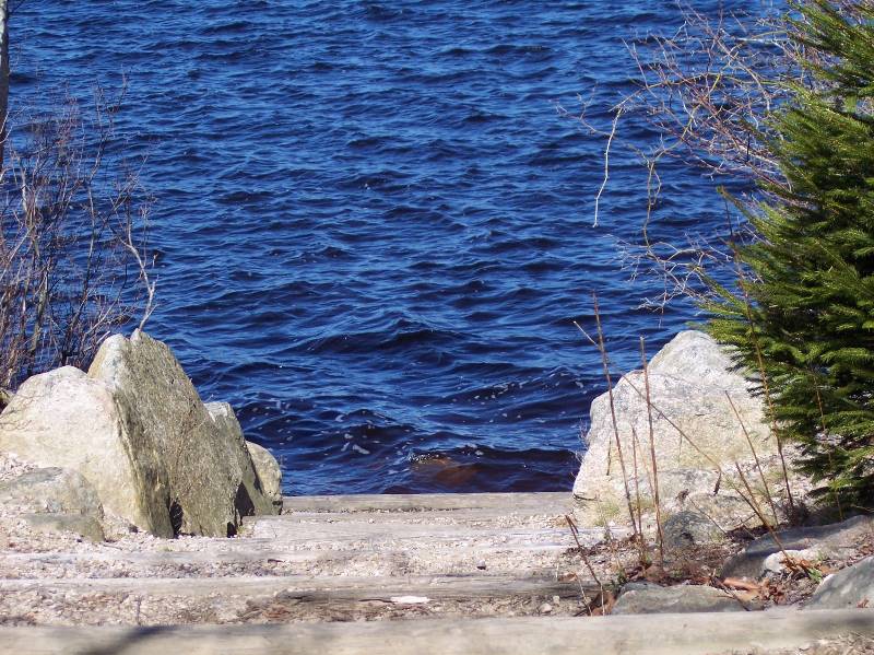 Lakeside scene at Camp Aquapaug with water, rocks, and trees.