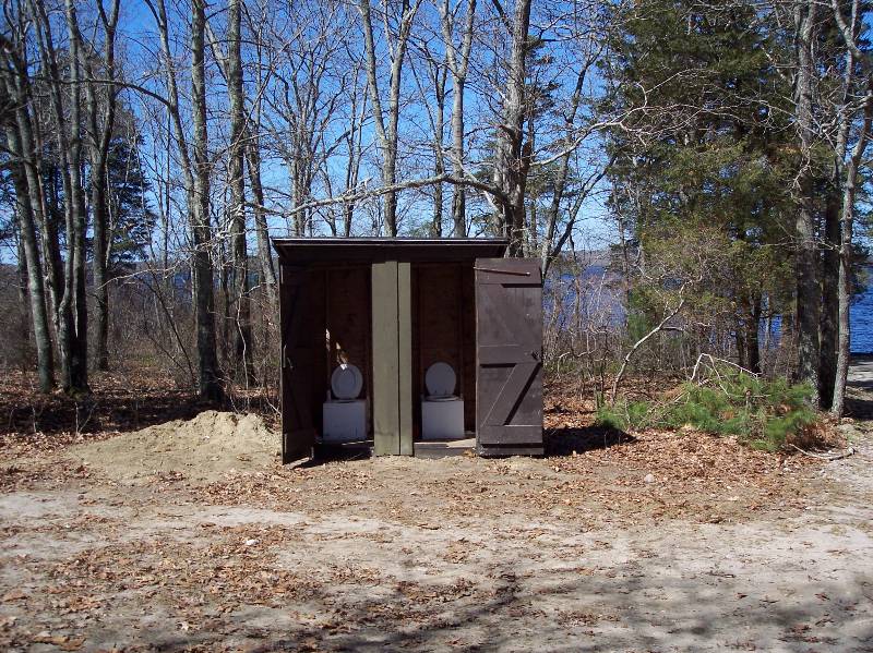 Outdoor restroom at Camp Aquapaug with rustic wooden structure and scenic forest setting.