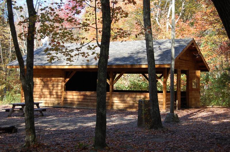 Wooden shelter at Camp Aquapaug surrounded by colorful fall foliage in a forest setting.