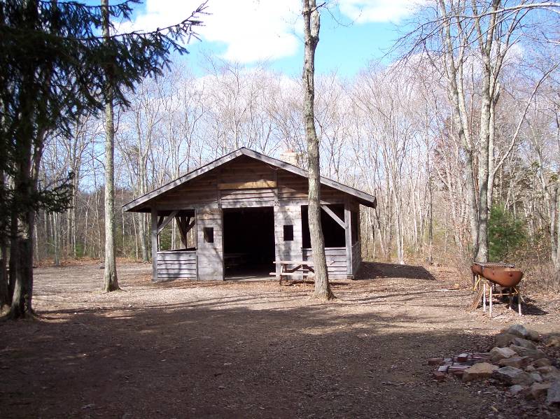 Rustic cabin at Camp Aquapaug, part of Narragansett Council, surrounded by trees.