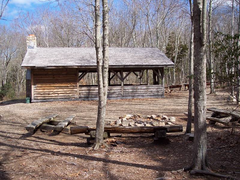 Rustic shelter at Camp Aquapaug with fire pit and wooded area.