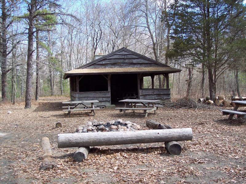 Outdoor pavilion at Camp Aquapaug with picnic tables and fire pit in a forested area.