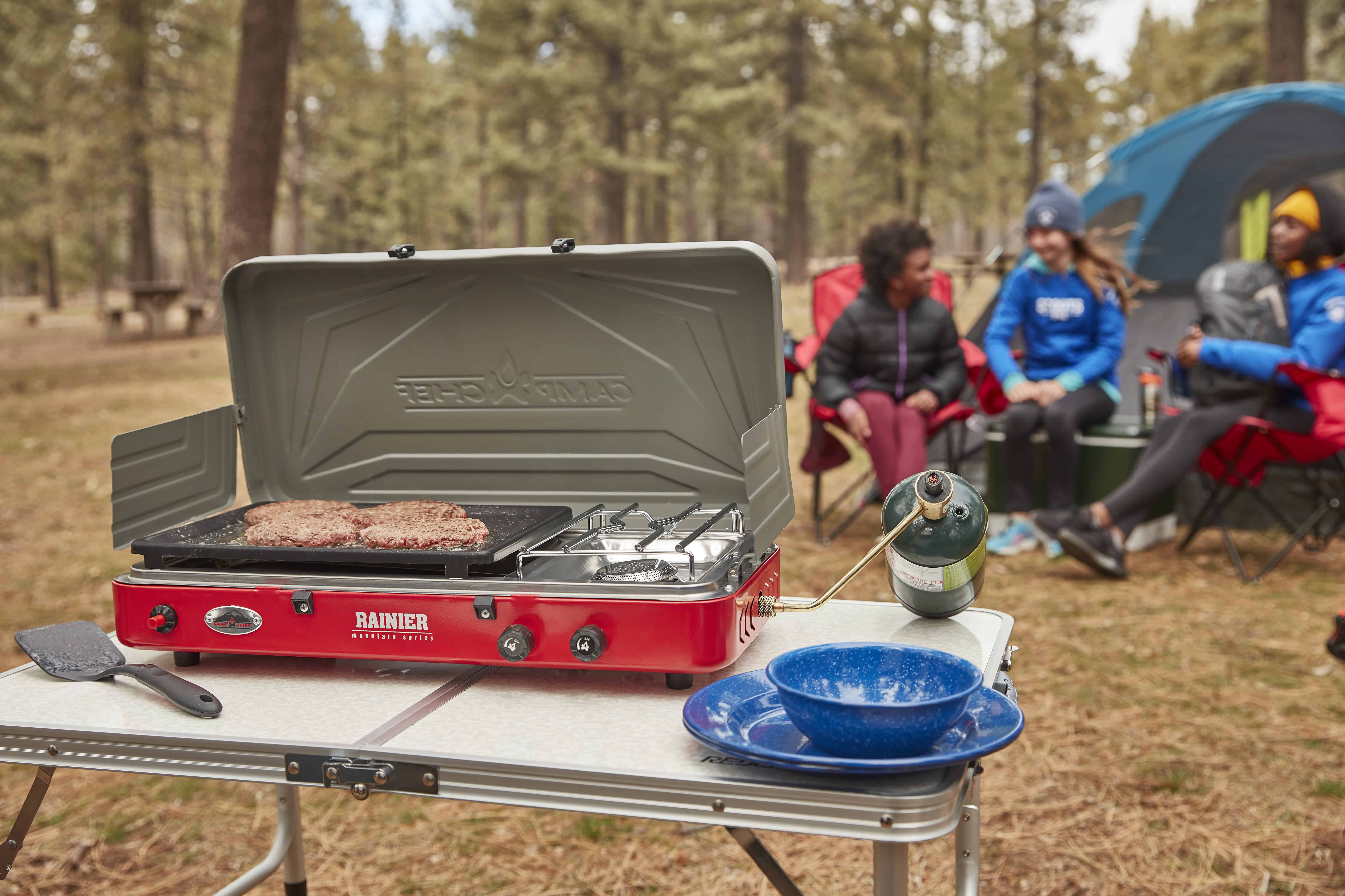 Outdoor camping grill with food and utensils for weekend camping trips.
