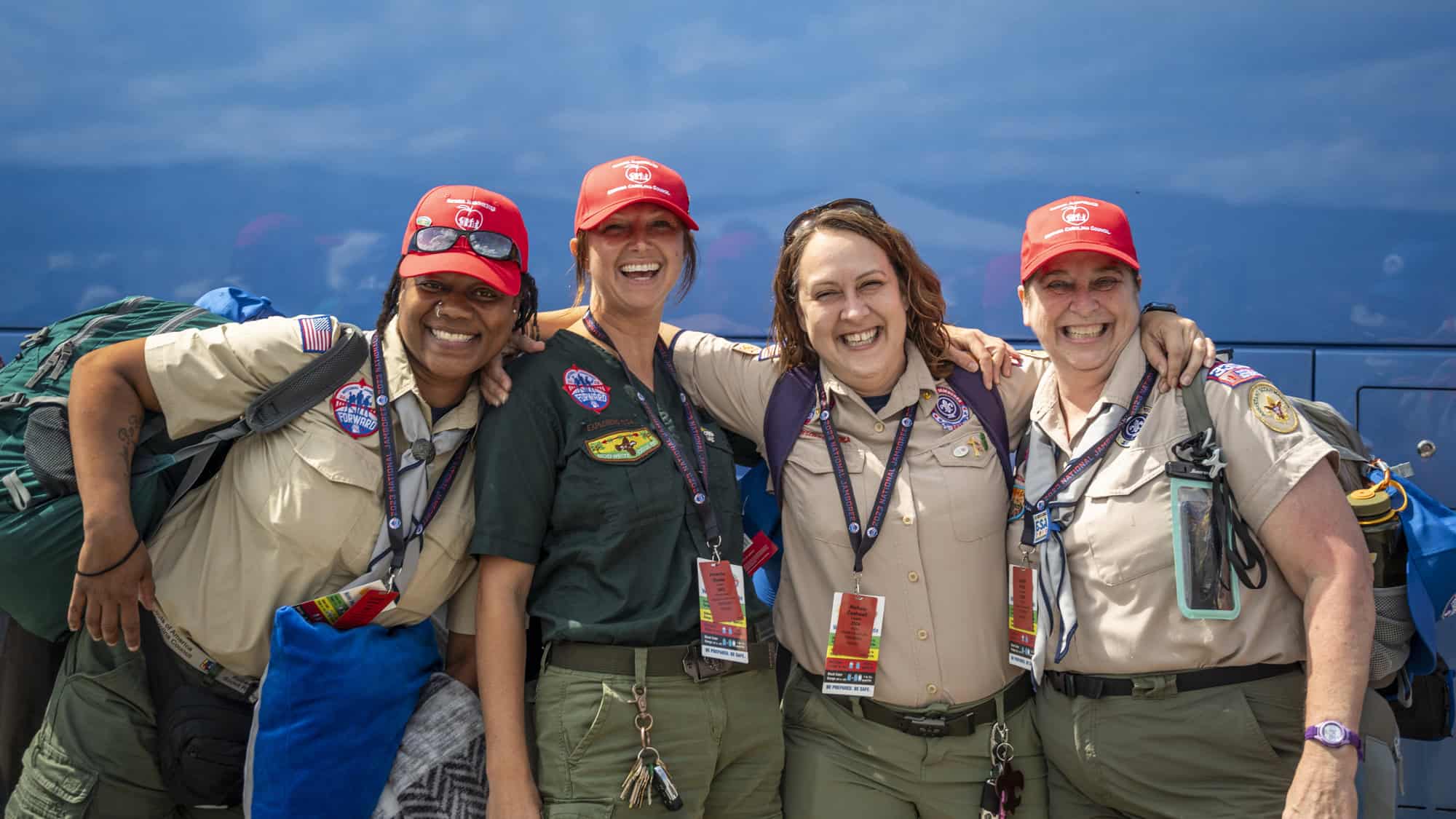 Girl Scout volunteers smiling at an outdoor event, wearing uniforms and hats.